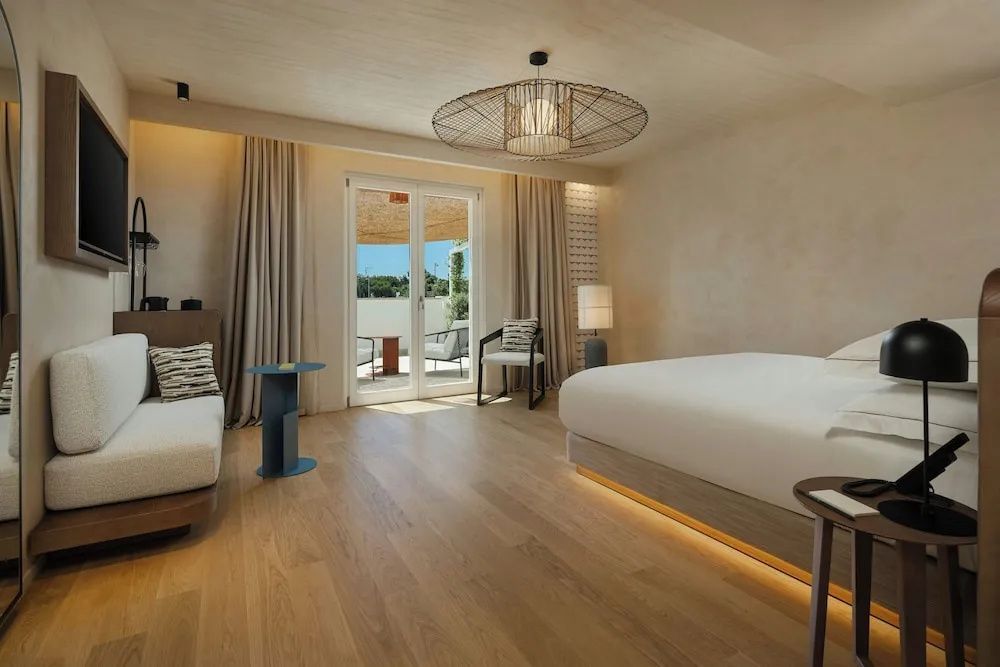 Modernes Hotelzimmer mit hellem Holzfußboden, Doppelbett und Zugang zur Terrasse.