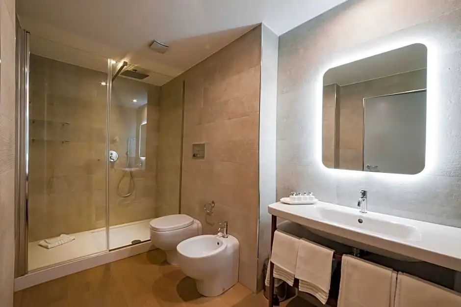 Badezimmer mit weißer Toilette, Bidet, Waschtisch und beleuchtetem Spiegel.