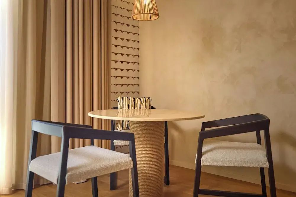 Sitzbereich im Hotelzimmer mit rundem Tisch, zwei Stühlen und einer Hängeleuchte.