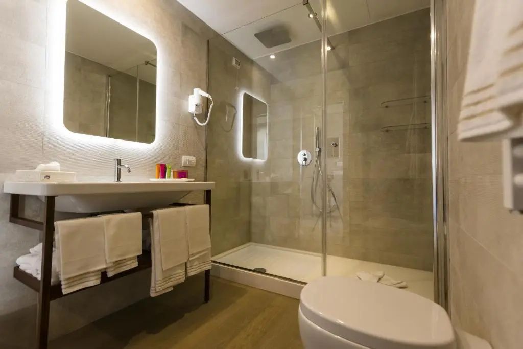 Badezimmer mit großem Wandspiegel, Duschkabine aus Glas und Handtüchern.