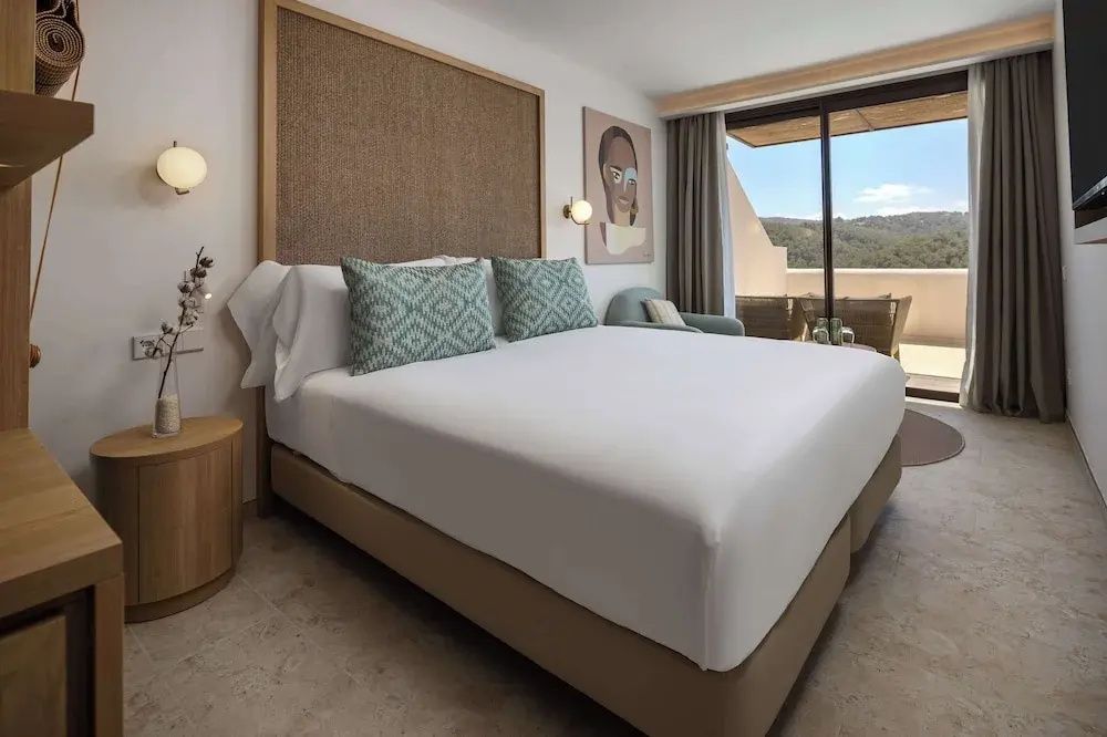 Helles Doppelzimmer mit Holz Kopfteil, grünem Kissen und Balkontür ins Freie.