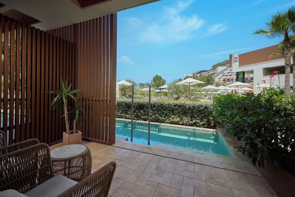 Blick von der überdachten Terrasse auf einen schmalen Pool und die Hotelanlage.