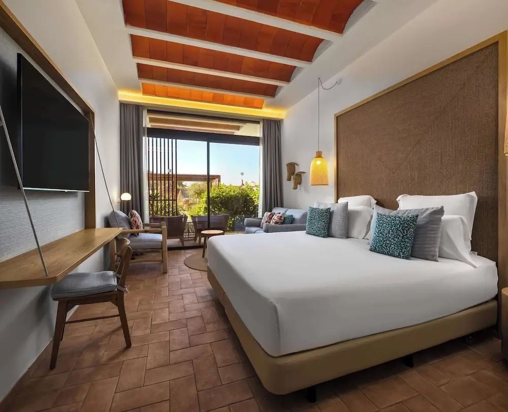 Modernes Hotelzimmer mit großem Doppelbett, Sitzecke und Terrasse zum Garten.