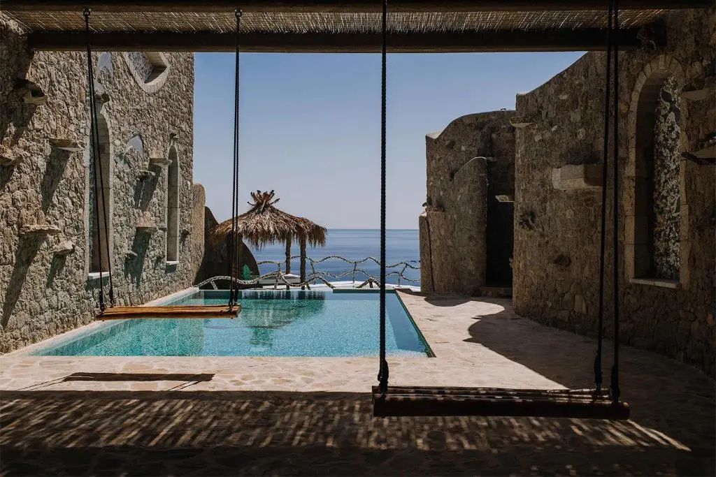 Blick von einer überdachten Terrasse mit Schaukel auf den Pool und das Meer.