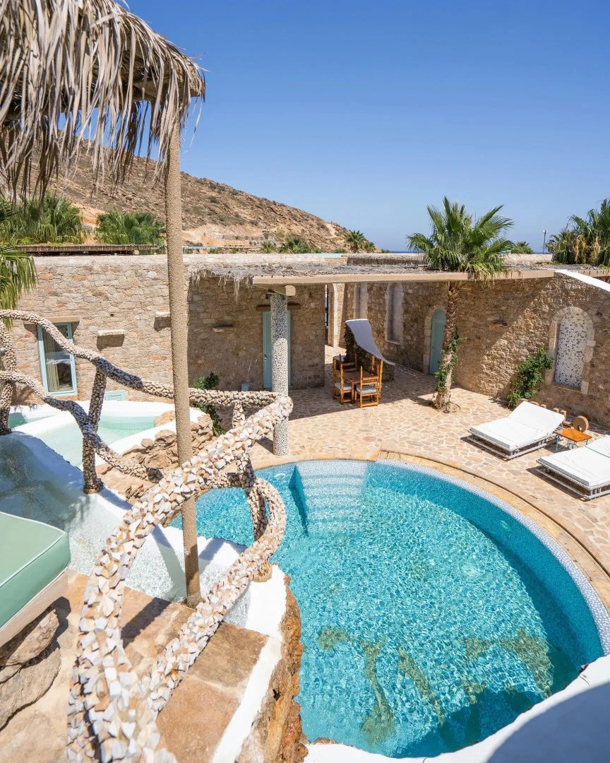 Privater Außenbereich mit rundem Pool, Sonnenliegen und Natursteinmauern.