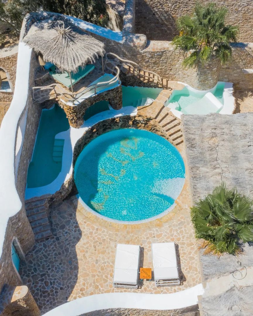 Vogelperspektive auf eine Poollandschaft mit Mosaikbecken, Liegen und Steinbrücken.