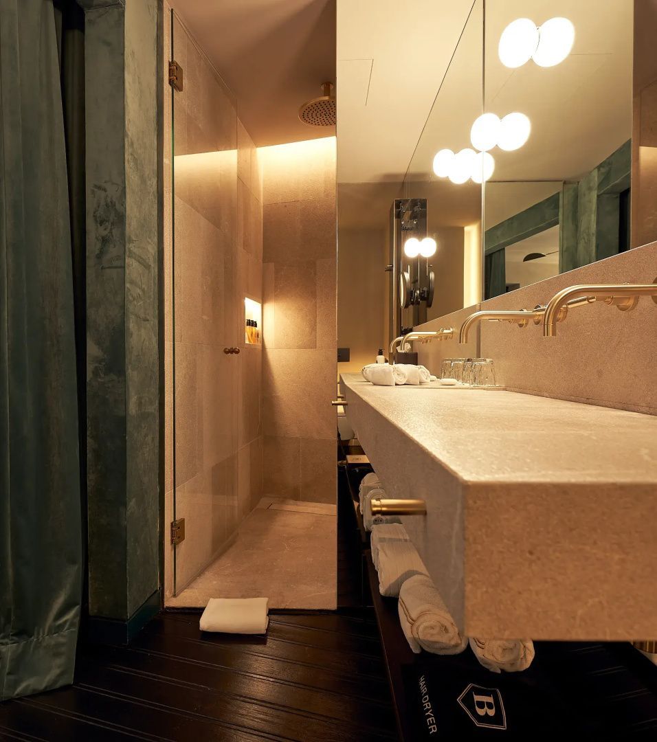Badezimmer mit breitem Steinwaschtisch, großem Spiegel und verglaster Dusche.