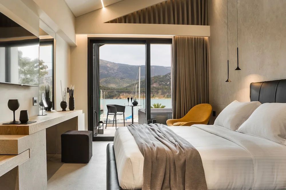 Blick vom Schlafzimmer über den Balkon auf ein Meeresbecken und Hügel.