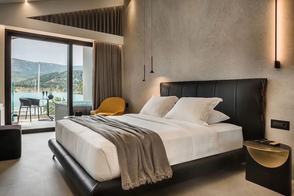 Doppelbett mit schwarzem Kopfteil, gelber Sessel und Balkontür mit Blick auf die Landschaft und das Meer.