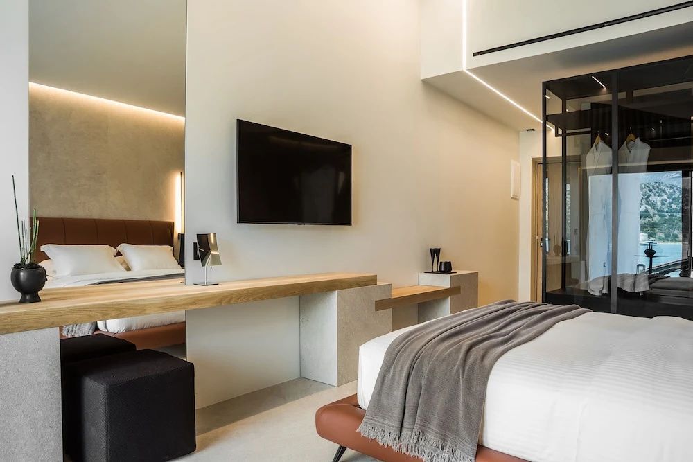 Schlafbereich mit Doppelbett, Schreibtisch und Wandfernseher in hellem Design.
