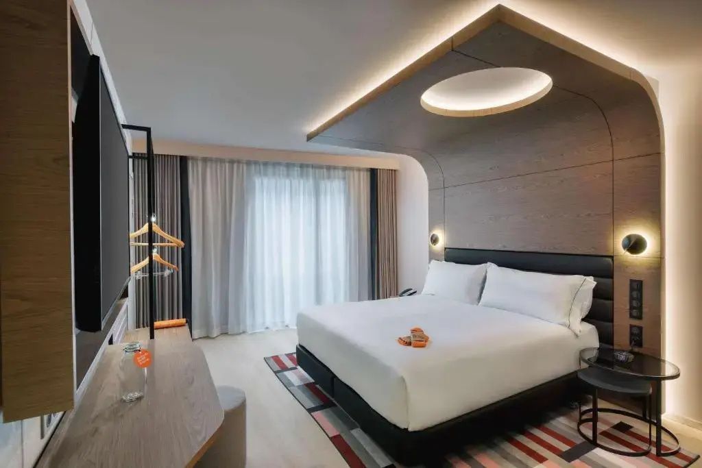 Modernes Hotelzimmer mit großem Doppelbett, holzverkleideter Decke und hellem Vorhang.