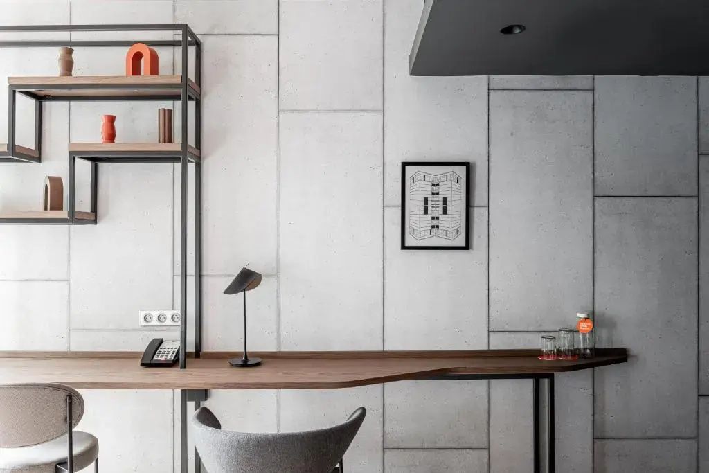 Arbeitsbereich im Zimmer mit Holzschreibtisch, schwarzer Lampe, Regal und dekorativer Betonwand.