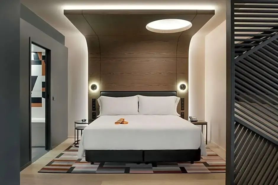 Doppelbett mit großem Holzpaneel an der Rückwand und zwei Nachttischen.