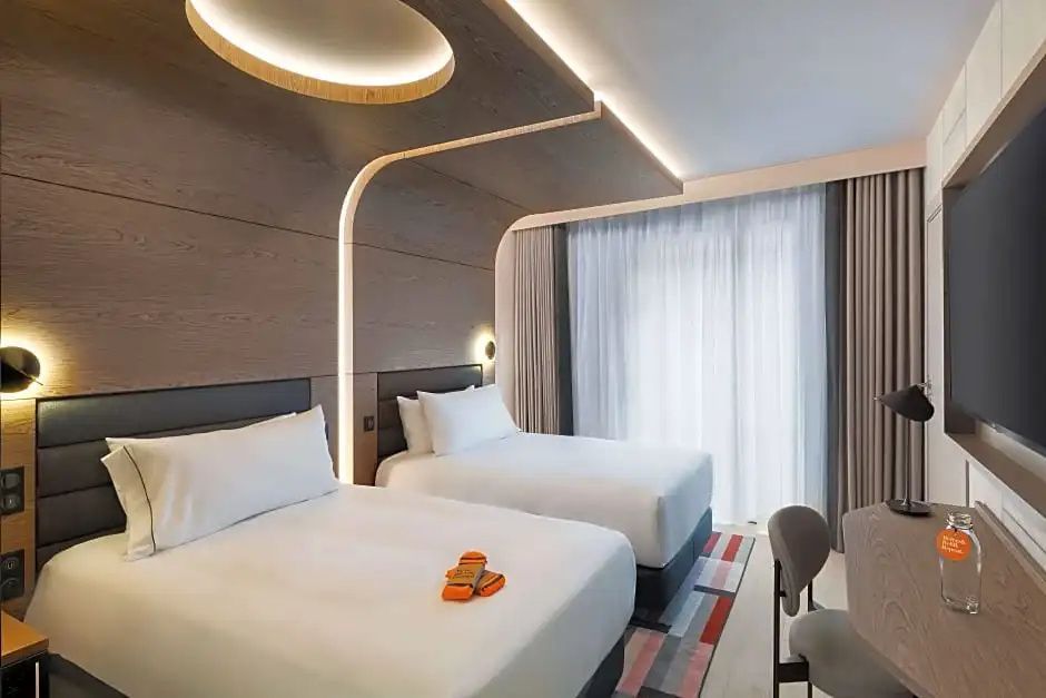 Hotelzimmer mit zwei Doppelbetten, moderner Holzkonstruktion an der Decke und Fenster.