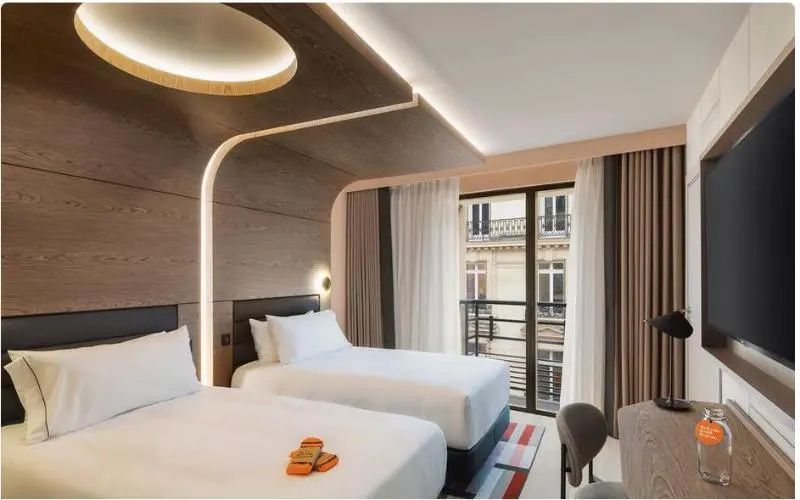 Modernes Zweibettzimmer mit Holzverkleidung an der Decke und Blick auf eine Pariser Fassade.