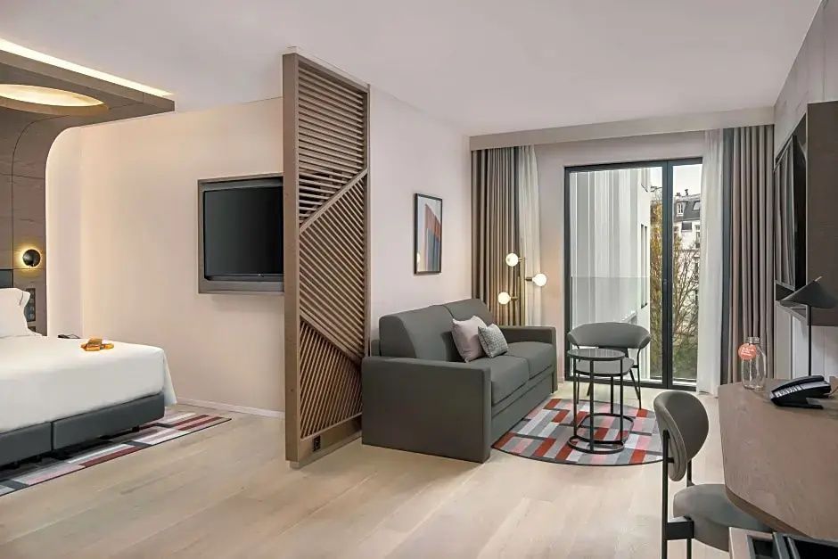 Modernes Wohnzimmer einer Suite mit grauem Sofa, Raumtrenner aus Holz und großem Fenster.