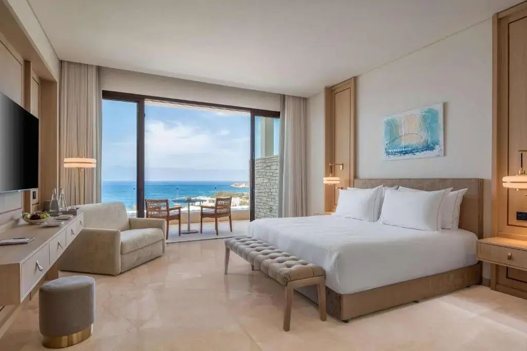 Hotelzimmer mit Blick durch die geöffnete Balkontür auf das blaue Meer.