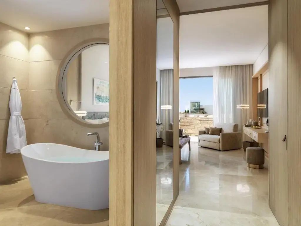 Offener Wohnbereich einer Suite mit freistehender Badewanne, hellem Fliesenboden und Blick zur Terrasse.