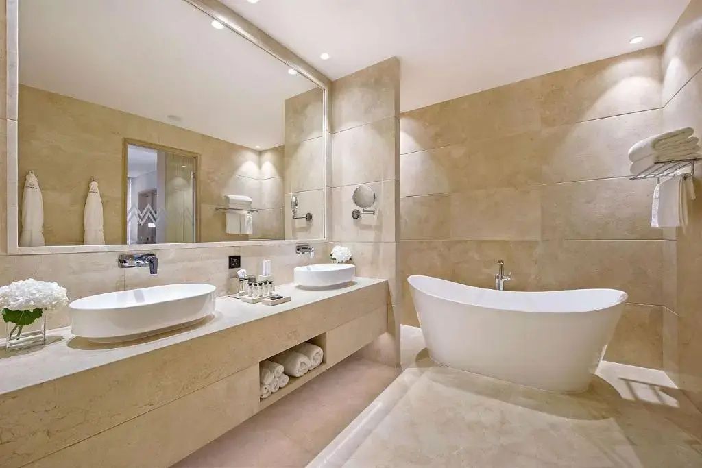 Badezimmer mit Doppelwaschtisch, großem Spiegel und einer freistehenden weißen Badewanne.