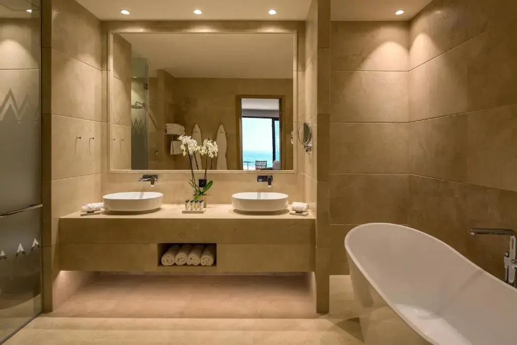 Großzügiges Badezimmer mit Doppelwaschbecken, großem Wandspiegel und einer Badewanne.