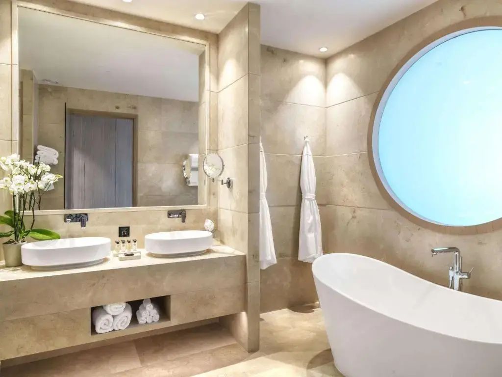 Badezimmer mit freistehender Badewanne, Doppelwaschtisch und kreisrundem Fenster.