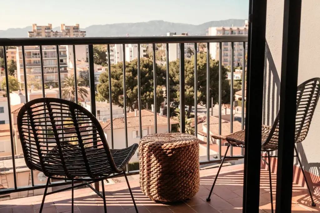 Balkon mit zwei Stühlen und einem Flechthocker mit Blick auf die Stadt und Berge.