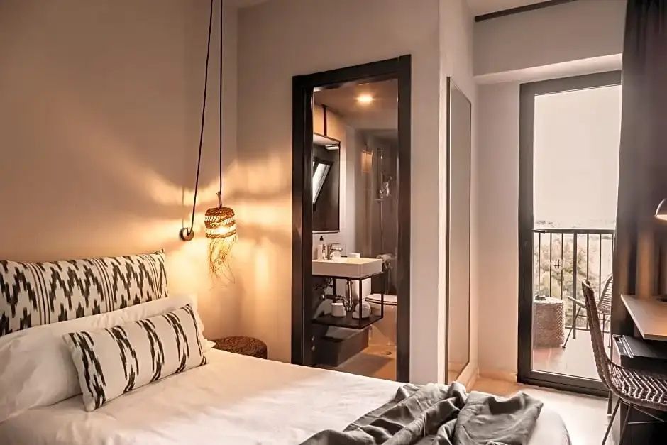 Modernes Hotelzimmer mit Doppelbett, getöntem Pendellicht und Blick ins Badezimmer.