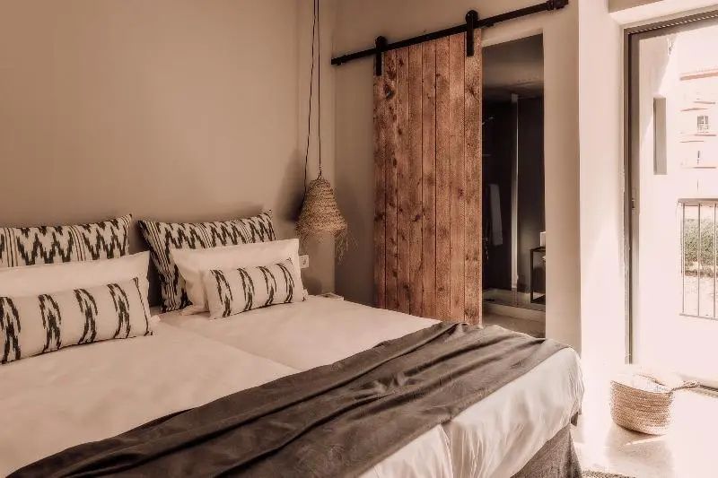 Doppelbett mit gemusterten Kissen und einer hölzernen Schiebetür zum Badezimmer.
