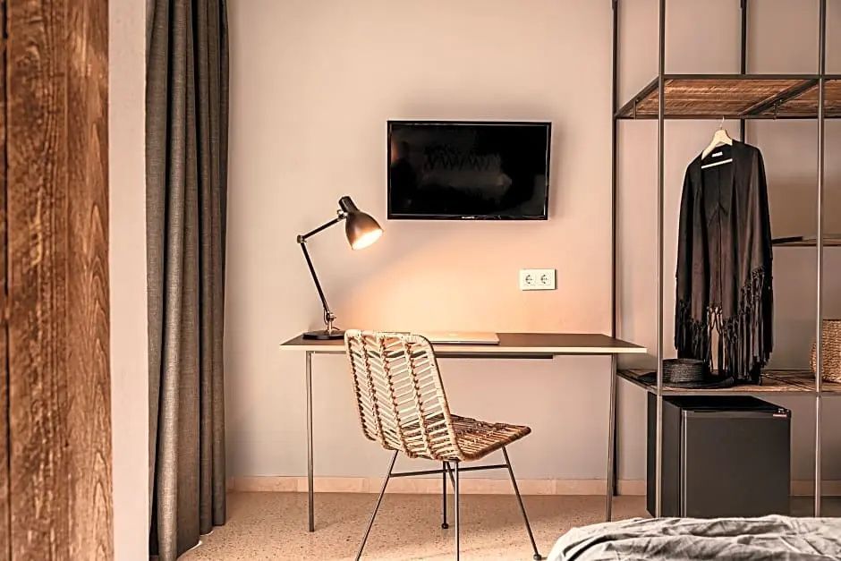 Schreibtisch mit Flechtstuhl, Tischlampe und an der Wand montiertem Fernseher.