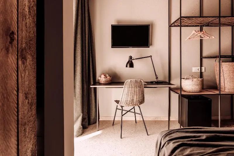 Schreibtischbereich mit Flechtstuhl, schwarzer Schreibtischlampe und Fernseher.