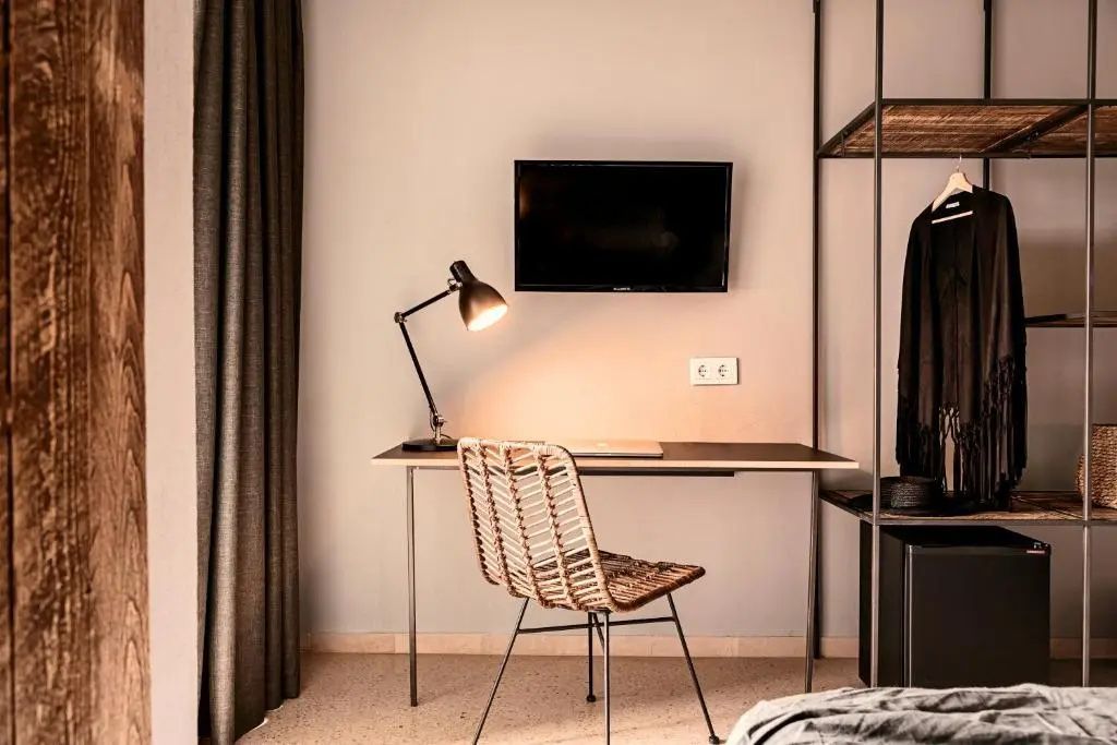 Arbeitsbereich im Hotelzimmer mit modernem Schreibtisch, Flechtstuhl, Lampe und Wandfernseher.
