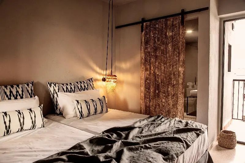 Hotelbett mit stimmungsvoller Beleuchtung und Holztür zum angrenzenden Bad.