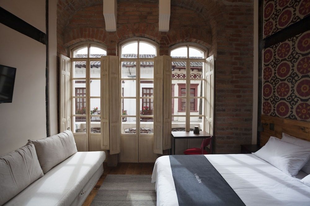 Schlafbereich mit Backsteinwand, weißem Bett und großen Bogenfenstern