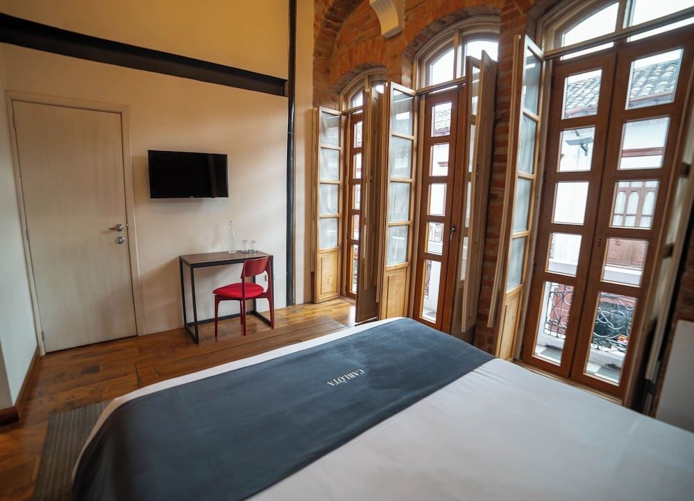 Hotelzimmer mit Bett, Wandfernseher und hohem Holzfenster zum Balkon