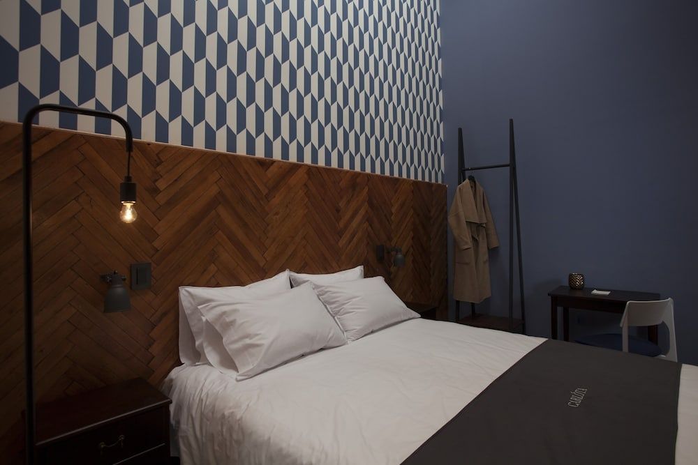 Doppelbett mit weißer Wäsche vor einer Wand mit Holz- und Geometriemuster.