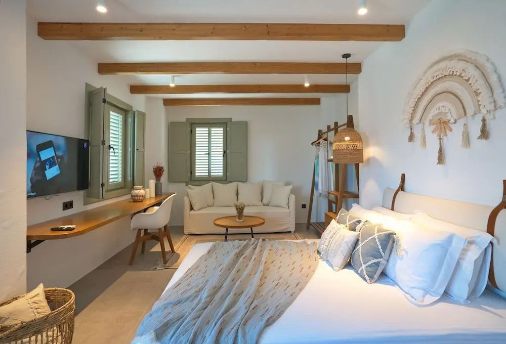 Hell eingerichtetes Hotelzimmer mit Doppelbett, Holzdecke, Schreibtisch und Sofa.