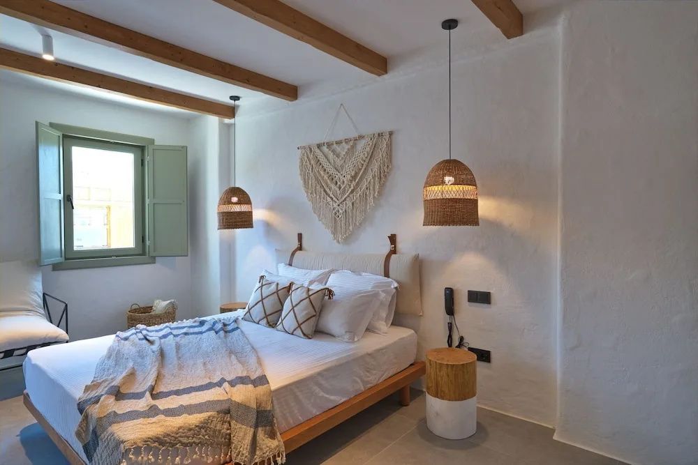 Schlafzimmer mit Holzbalkendecke, Doppelbett, Makramee-Wandbehang und Flechtlampen.