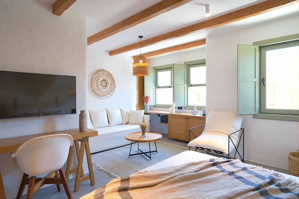 Wohnbereich eines Hotelzimmers mit hellem Sofa, Sessel, Holzcouchtisch und TV.