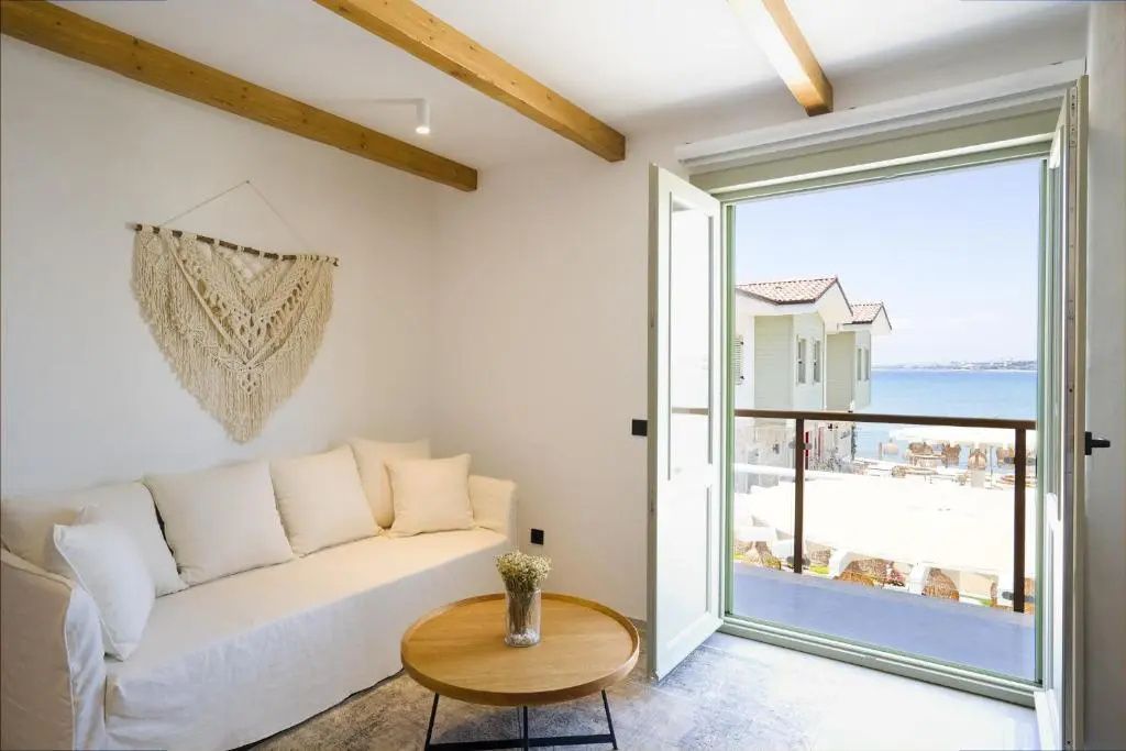 Wohnbereich mit weißem Sofa, Makramee-Wandteppich und geöffneter Balkontür mit Meerblick.