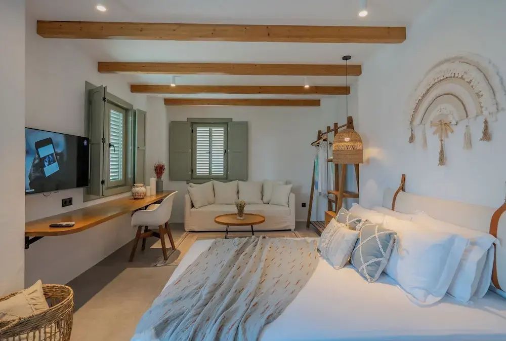 Helles Hotelzimmer mit Doppelbett, weißem Sofa, Holzschreibtisch und Holzbalken an der Decke.