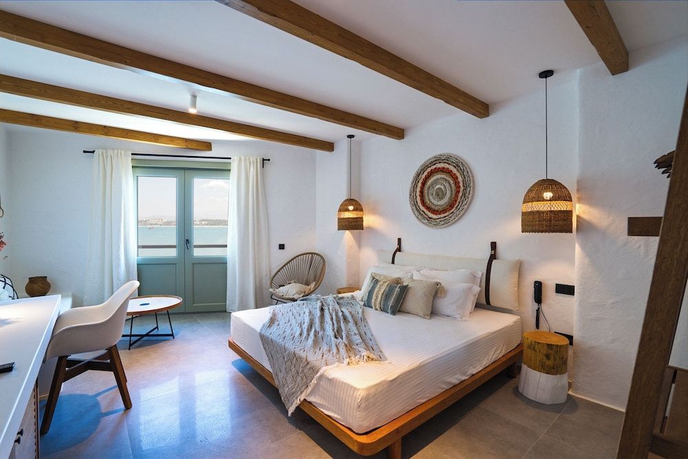 Hell eingerichtetes Schlafzimmer mit Holzbalken an der Decke und Blick aufs Meer.