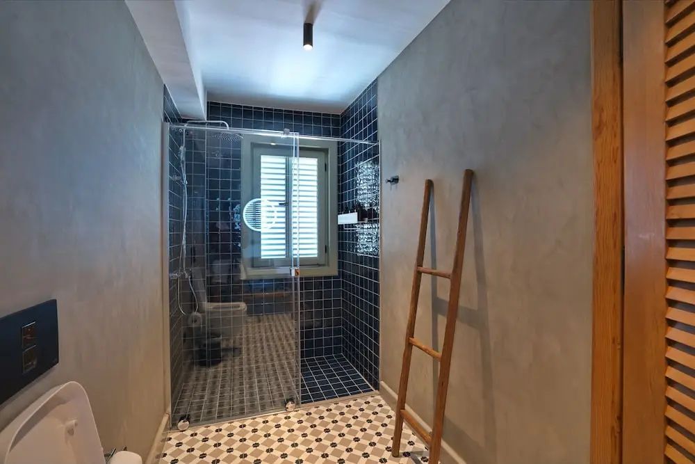 Badezimmer mit begehbarer Glasdusche, blauen Wandfliesen und dekorativer Holzleiter.