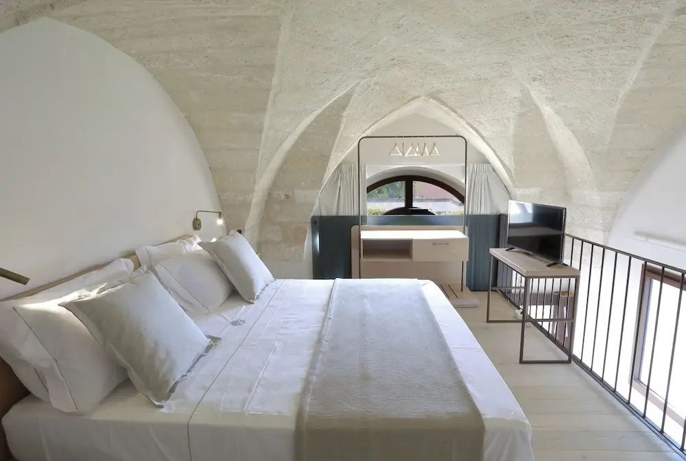 Doppelbett in einem Zimmer mit historischem Kreuzgewölbe aus Naturstein und Fernseher.