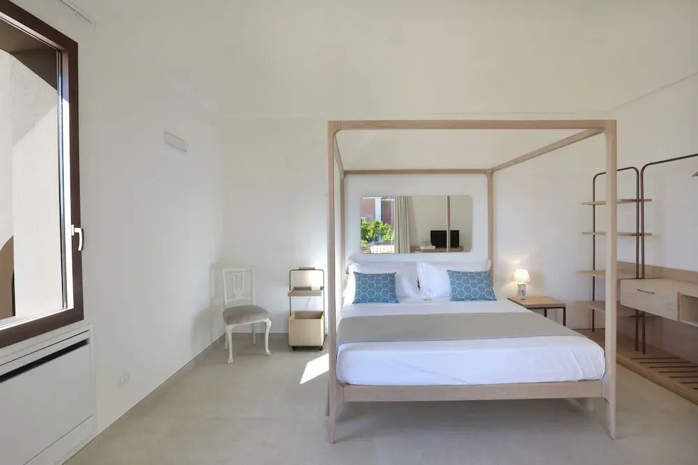 Schlicht eingerichtetes Hotelzimmer mit einem Himmelbett aus Holz und Spiegel.