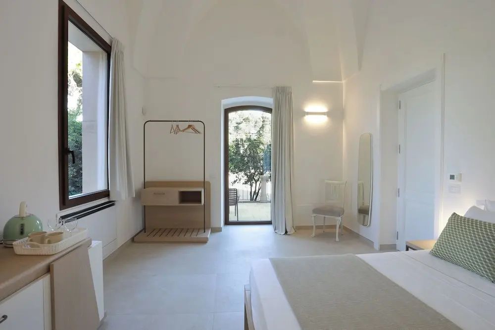 Weißes Zimmer mit hoher Gewölbedecke, offenem Kleiderständer und Tür mit Blick ins Grüne.