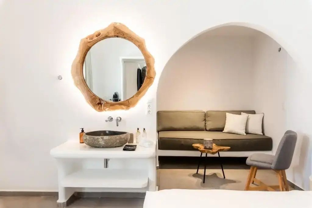 Innenraum einer Suite mit einem Steinwaschbecken, runden Holzspiegel und Sofa in einer Nische.