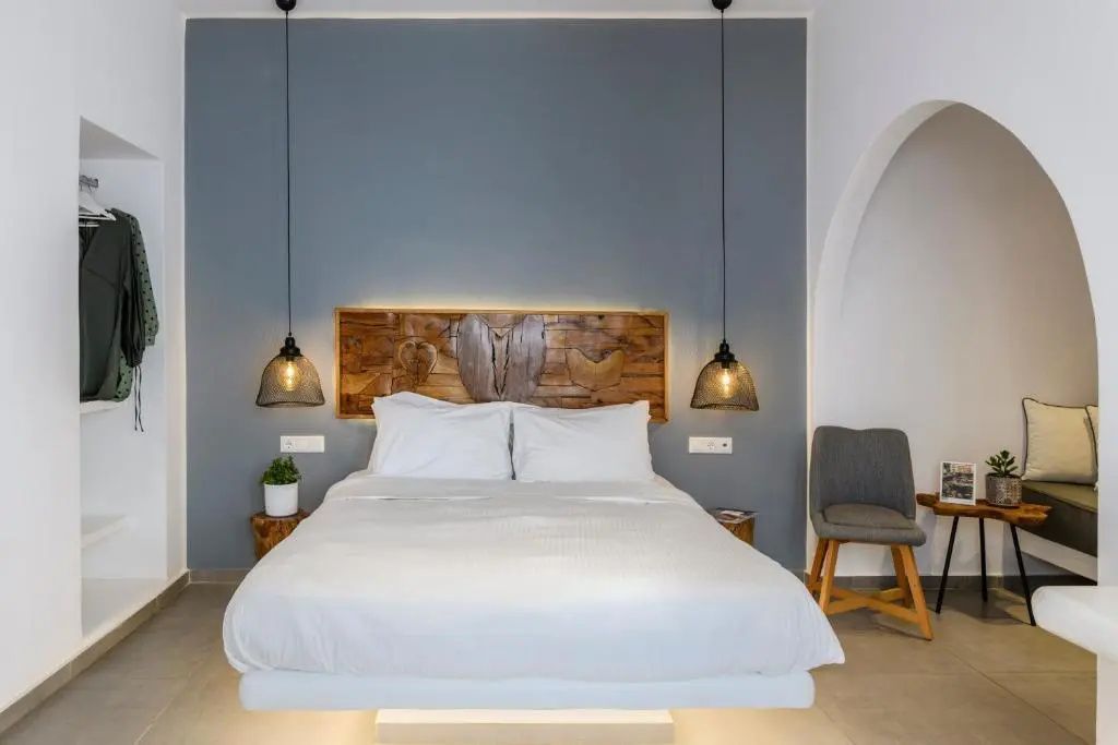 Doppelbett mit weißer Bettwäsche, Kopfteil aus Holz und Hängeleuchten vor grauer Wand.