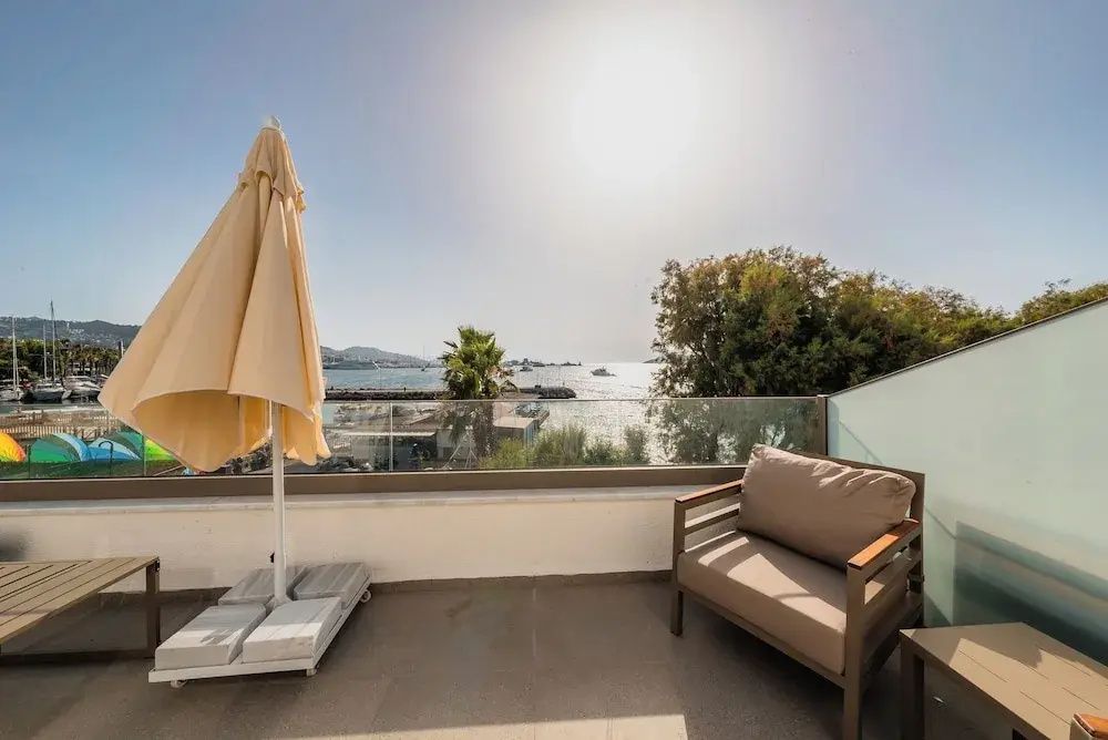 Sonnige Terrasse mit Sessel, Sonnenschirm und Blick auf das Meer und den Hafen.