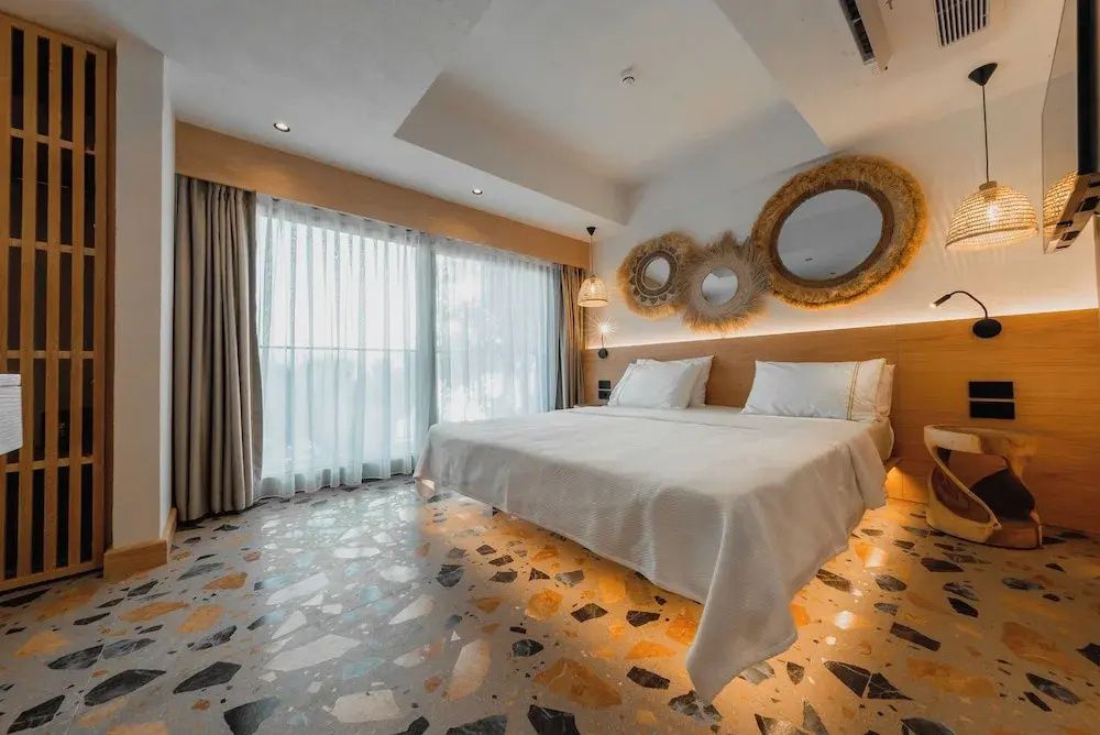 Helles Hotelzimmer mit Doppelbett, buntem Terrazzoboden und dekorativen Spiegeln an der Wand.