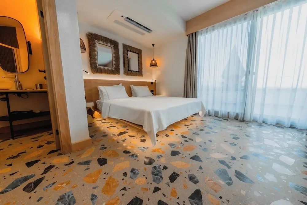 Modernes Hotelzimmer mit Doppelbett, Terrazzoboden, indirekter Beleuchtung und Holzdekor.